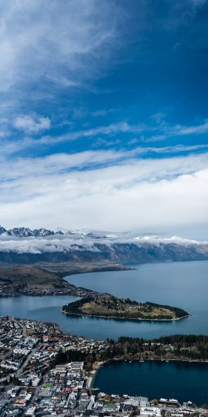 Stunning aerial view of Queenstown with Lake Wakatipu and distant mountains under a vibrant blue sky.
